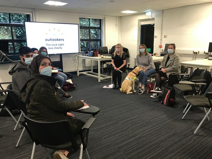 Image shows Sam with guide dog Annie talking with a group of students.